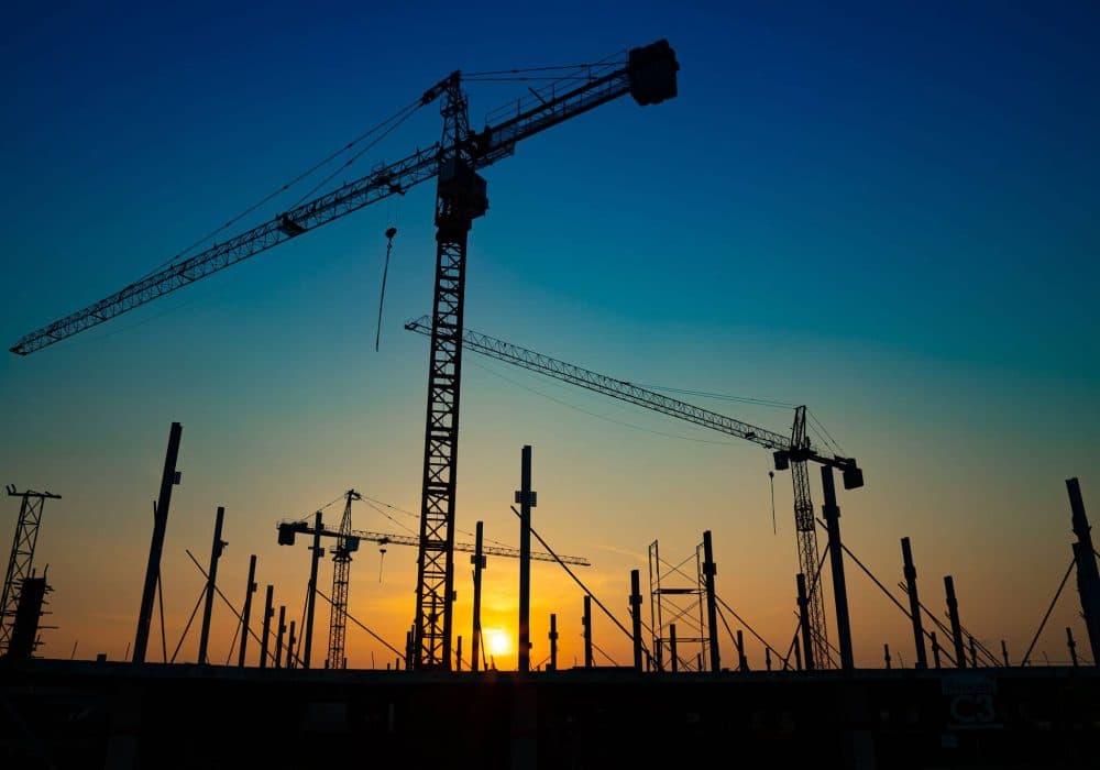 New construction site with cranes on orange sunset, sunrise sky background. Steel frame structure, structural steel beam build large buildings at construction site . construction machinery.